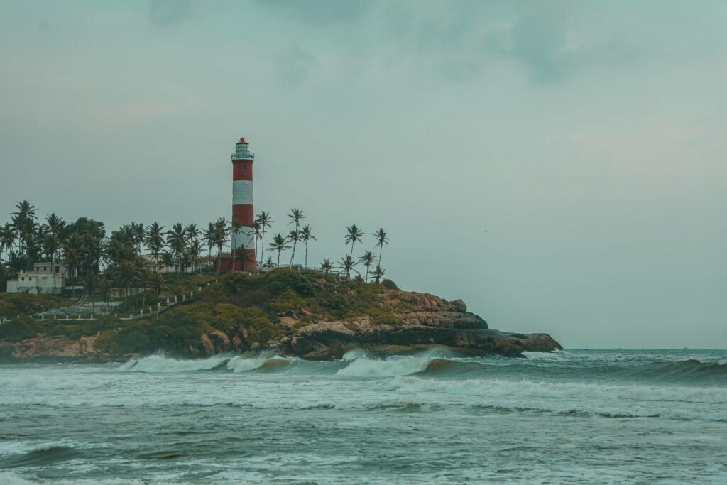 Scenic view of Kovalam Beach lighthouse with palm trees and rocky shore in Kerala, India.